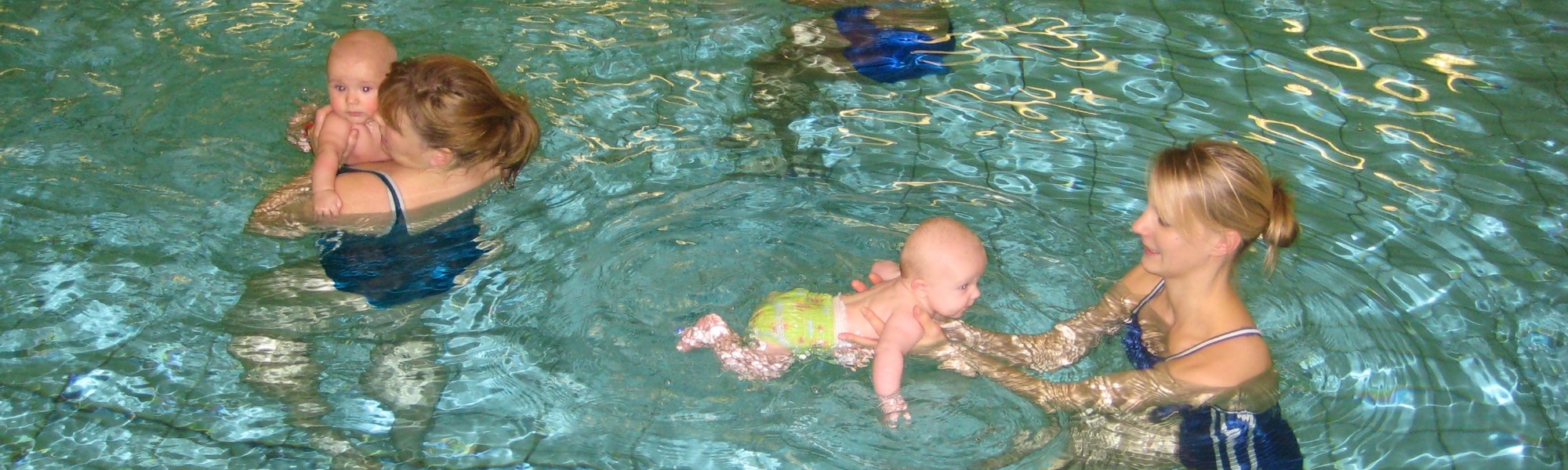 Kursteilnehmerinnen im Wasser, die ein Baby im Arm halten